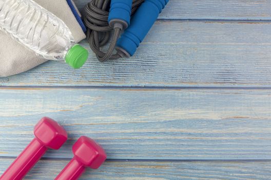 Top or flat lay view of dumbbells, towel, water and skipping rope with copy space area on blue wooden background. Healthy concept. Selective focus.