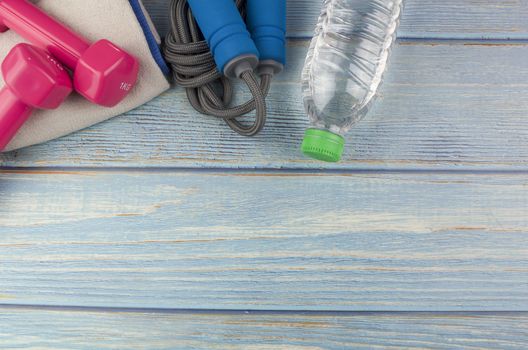 Top or flat lay view of dumbbells, towel, water and skipping rope with copy space area on blue wooden background. Healthy concept. Selective focus.