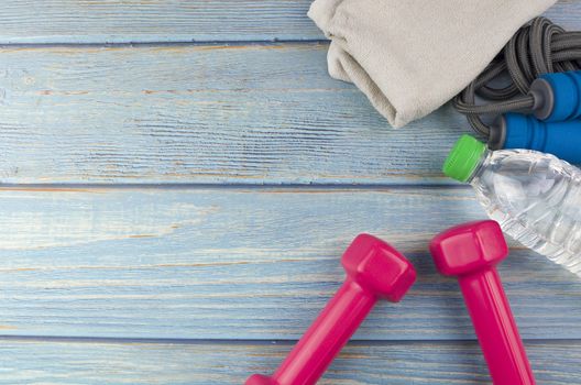 Top or flat lay view of dumbbells, towel, water and skipping rope with copy space area on blue wooden background. Healthy concept. Selective focus.