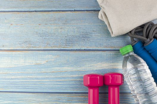 Top or flat lay view of dumbbells, towel, water and skipping rope with copy space area on blue wooden background. Healthy concept. Selective focus.