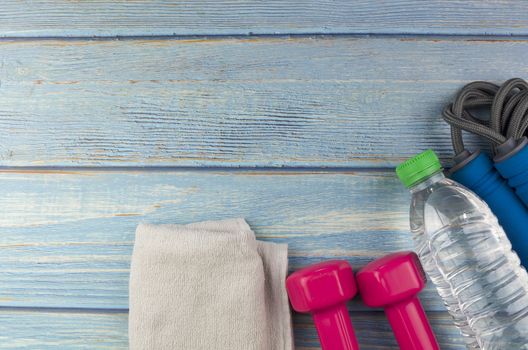 Top or flat lay view of dumbbells, towel, water and skipping rope with copy space area on blue wooden background. Healthy concept. Selective focus.