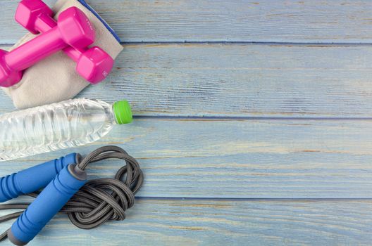 Top or flat lay view of dumbbells, towel, water and skipping rope with copy space area on blue wooden background. Healthy concept. Selective focus.