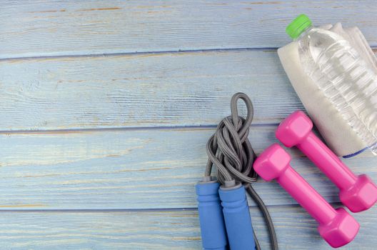 Top or flat lay view of dumbbells, towel, water and skipping rope with copy space area on blue wooden background. Healthy concept. Selective focus.