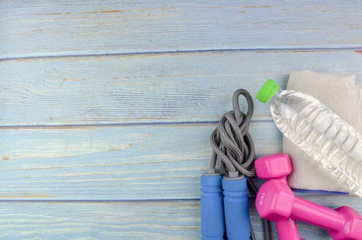 Top or flat lay view of dumbbells, towel, water and skipping rope with copy space area on blue wooden background. Healthy concept. Selective focus.