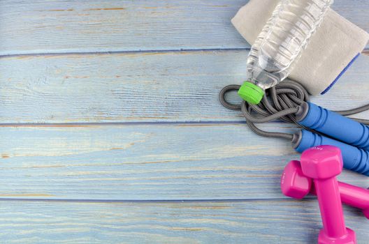 Top or flat lay view of dumbbells, towel, water and skipping rope with copy space area on blue wooden background. Healthy concept. Selective focus.