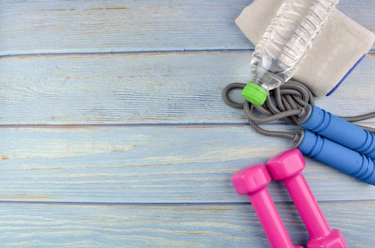 Top or flat lay view of dumbbells, towel, water and skipping rope with copy space area on blue wooden background. Healthy concept. Selective focus.