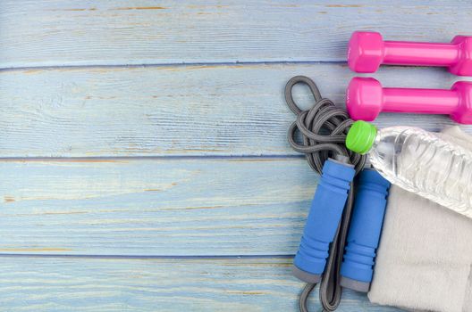 Top or flat lay view of dumbbells, towel, water and skipping rope with copy space area on blue wooden background. Healthy concept. Selective focus.