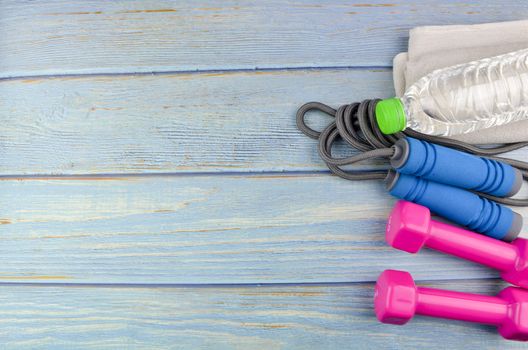 Top or flat lay view of dumbbells, towel, water and skipping rope with copy space area on blue wooden background. Healthy concept. Selective focus.