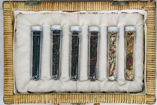 Six tube of different leaf teas collection in wicker basket.