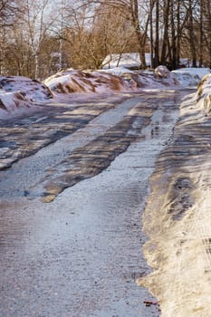 winter road covered with snow and ice with puddles and ruts, sunny day