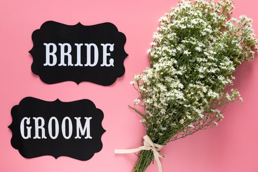 Bride and Groom text sign on pink background decorated with white flower bouquet, vintage style. wedding sign concept