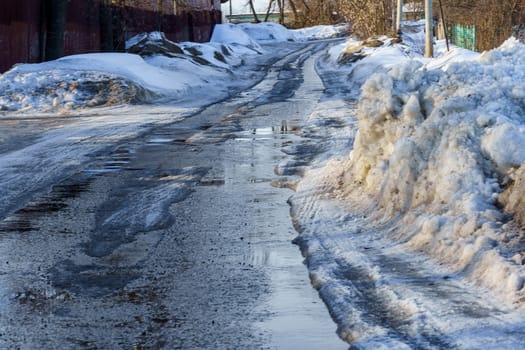 winter road covered with snow and ice with puddles and ruts, sunny day