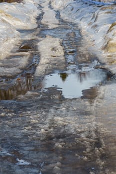 winter road covered with snow and ice with puddles and ruts, vertical shot