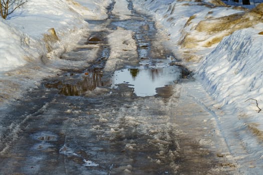 winter road covered with snow and ice with puddles and ruts, sunny day