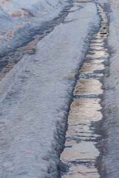 winter road covered with snow and ice with puddles and ruts, vertical shot