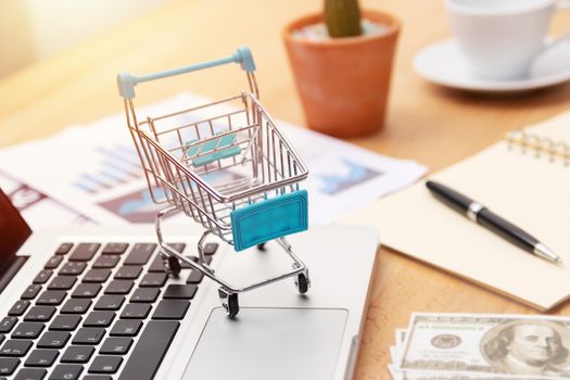 E-commerce business concept. shopping cart on laptop keyboard with marketing chart and money cash note. shopping online and transaction via internet technology, marketing strategy.