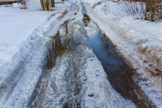 winter road covered with snow and ice with puddles and ruts, sunny day