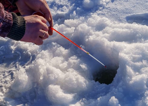hands of a fisherman, a winter fishing pole and a hole in the ice, an ice fishing plot