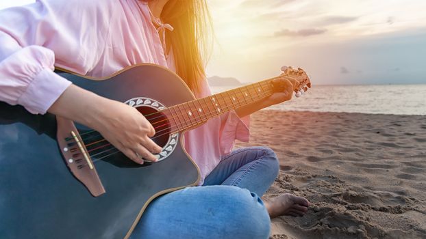 woman's hands playing acoustic guitar, capture chords by finger on sandy beach at sunset time. playing music concept