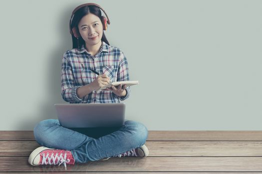 female student relaxed sitting on a wooden floor at home and watching training online course and listening it with headphones from compute laptop. online education service with modern study technology