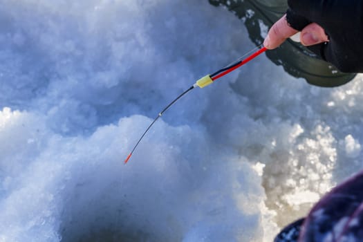 winter rod and angler's hands over the hole in the ice