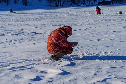 angler on ice with fishing rod on a sunny winter day