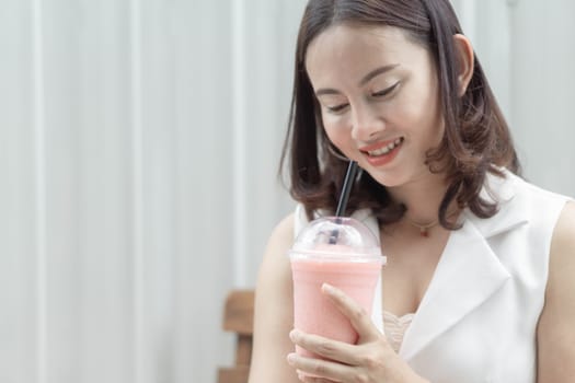 Closeup woman drinking strawberry smoothie and cake with green nature background, selective focus