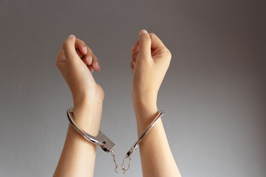 closeup of two hands of a man with handcuffs on a grey vignette background