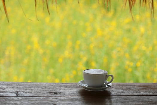 White coffee cup on wooden table with bokeh yellow flower field