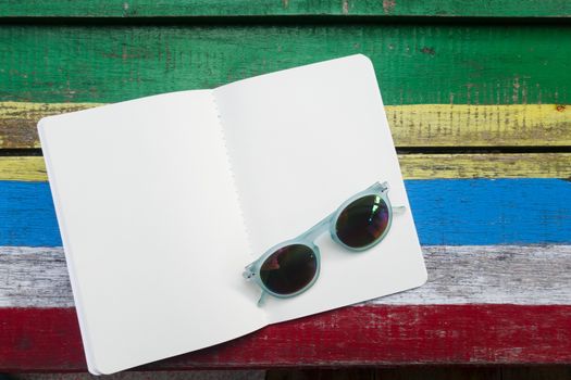 open blank white page book on colorful wooden background , decoration with sunglass fashion