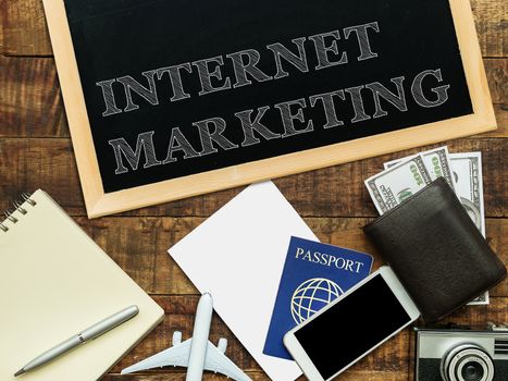 internet marketing handwritten with white chalk on a blackboard, money wallet , notebook and smartphone on a wooden background