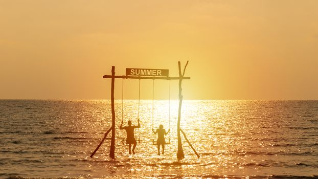 silhouette of happy couple playing swing over the sea with summer sign. happy summer vacation concept