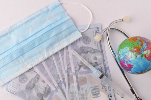 Medical face mask, stethoscope, syringe, world globe and banknotes on white background. Medical concept. Selective focus.