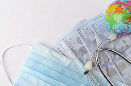 Medical face mask, stethoscope, syringe, world globe and banknotes on white background. Medical concept. Selective focus.