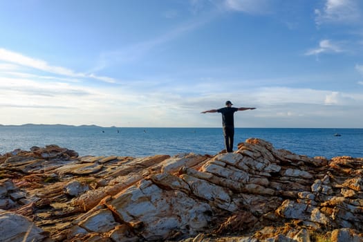 man stands his arms on a rock by the sea at Khao Laem Ya, Rayong, Thailand.