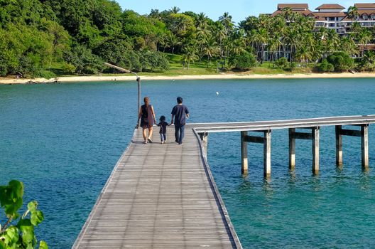 Family holiday with parents carrying children along the sea-side bridge at Khao Laem Ya National Park, Rayong, Thailand.