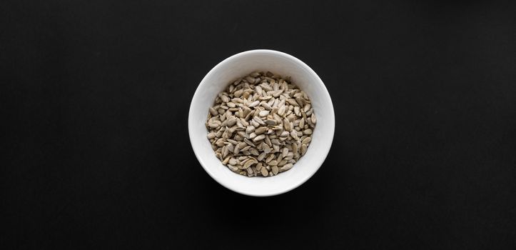 Sunflower seeds in a small plate on the black table. Healthy vegetarian protein nutritious food