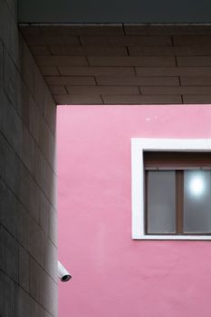 Composition of parallel and perpendicular lines with a window and a security camera on a magenta wall, framed with blocks of gray cement.