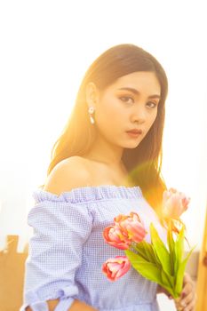 beautiful Asian women in blue dress with red tulip flowers in hands with sunlight in the morning from window