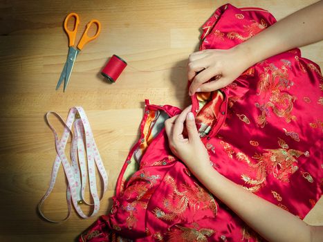 top view of cropped female hands sewing Cheongsam dress with needle at seamstress workplace with sewing equipment