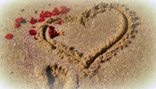 In the sand painted heart with scattered sheets of a rose and a small footprint
