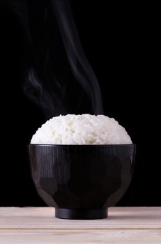 Cooked rice in japanese bowl on black background with smoke, steamed rice