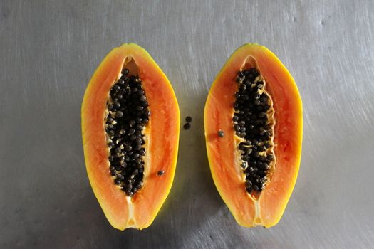 Papaya fruit cut in half on the kitchen table. Gray metal kitchen table background.