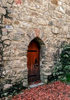 old locked wooden door in a stone wall with green moss and fallen autumn yellow leaves