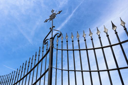 Wrought iron gate with cross against blue sky