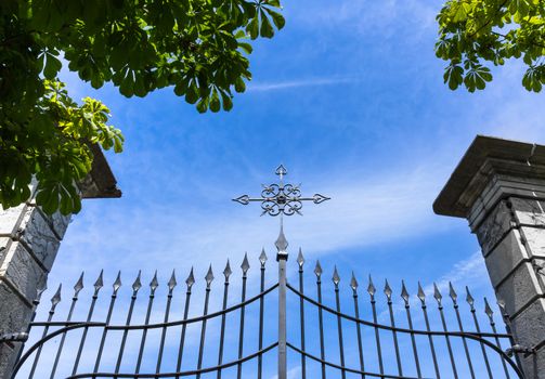 Wrought iron gate with cross against blue sky