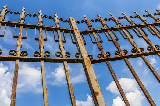 Old gate rusty in the foreground on blue sky background with clouds. Ideal for renovation concepts.