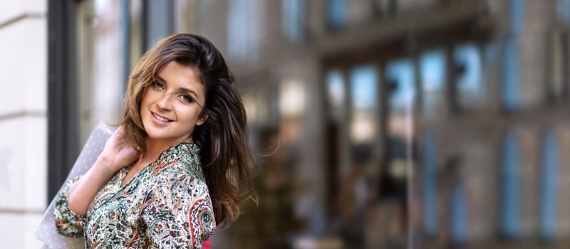 Advertisement banner - happy young woman with shopping bags is looking at camera and smiling while doing shopping in the city ( copy space)