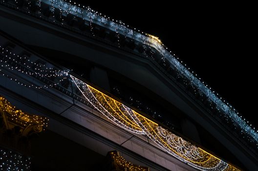 fragment of the facade and roof of a vintage building with colored lights decoration isolated on black background at night