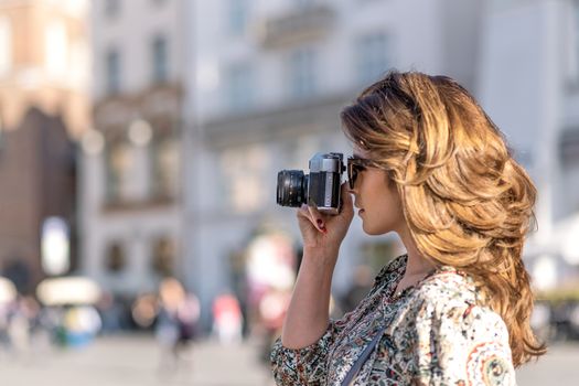 Vacation photographer concept - beautiful and attractive woman holding a retro SLR camera and shooting famous landmarks of a historic city (copy space)